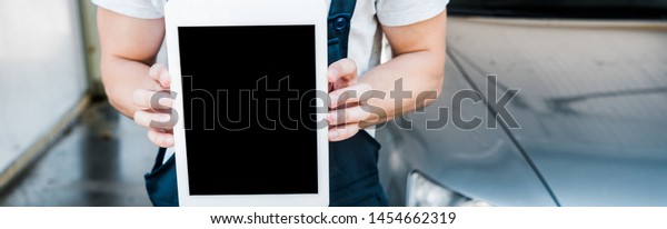 panoramic shot of car cleaner holding digital tablet\
with blank screen 