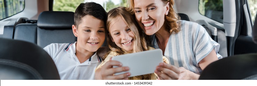 Panoramic Shot Of Cheerful Family Taking Selfie On Smartphone In Car 