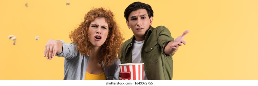 Panoramic Shot Of Emotional Irritated Couple Watching Bad Movie And Throwing Popcorn, Isolated On Yellow