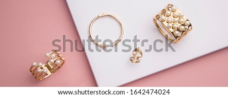 panoramic shot of flat lay of golden bracelets and ring on pink and white paper background
