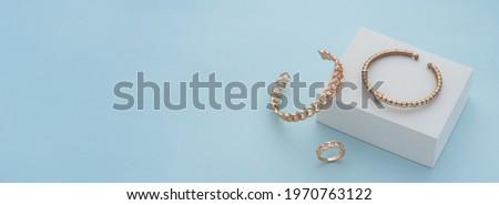 Panoramic shot of golden bracelets and ring on white box on blue background with copy space