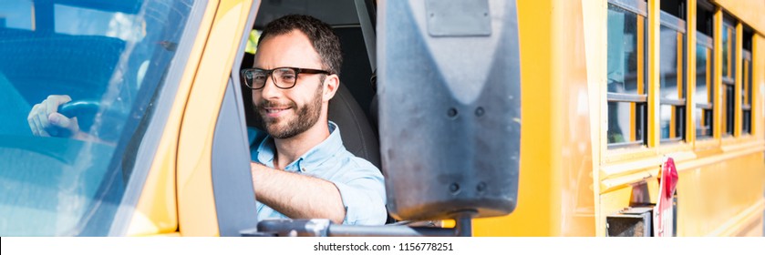 Panoramic Shot Of Handsome School Bus Driver Smiling And Driving