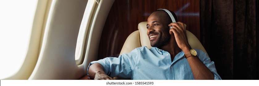 panoramic shot of happy african american man listening music in private plane 