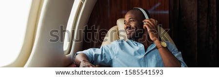 panoramic shot of happy african american man listening music in private plane 