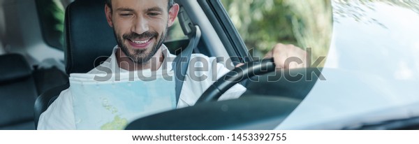 panoramic shot of happy driver sitting in car and\
looking at map 
