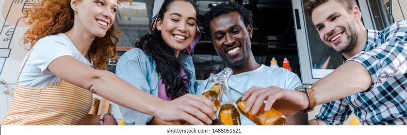 Panoramic Shot Of Happy Multicultural Friends Clinking Bottles With Beer Near Food Truck 