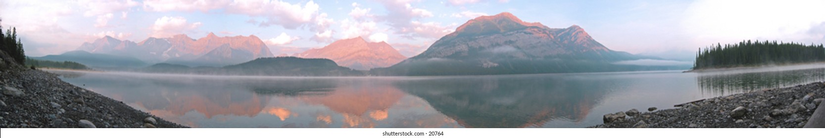 A panoramic shot of a lake with trace amounts of fog in the rocky mountains.