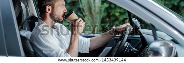panoramic shot of man drinking coffee to go while\
driving car 