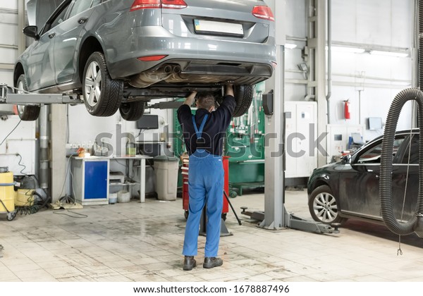 Panoramic shot of\
the mature car mechanic checking and repairing a lifted car in his\
garage. Checking and refilling the gearbox oil reservoir. Old car\
mechanics and repair\
concept.