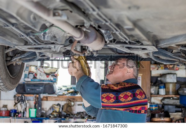\
Panoramic shot of an old car mechanic checking and repairing a\
lifted car in his garage. Checking and refilling the gearbox oil\
reservoir. Old car mechanics and repair\
concept.