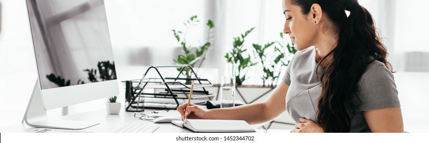 toma panorámica de una mujer embarazada sentada detrás de una mesa con ordenador, teclado y bandeja de documentos, escribiendo notas y sosteniendo el vientre 