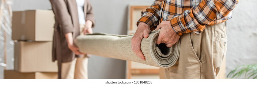 Panoramic Shot Of Senior Couple Rolling Carpet In New House, Moving Concept