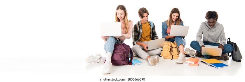 Panoramic shot of smiling multicultural teenagers using laptops near backpacks and books on white background - Powered by Shutterstock