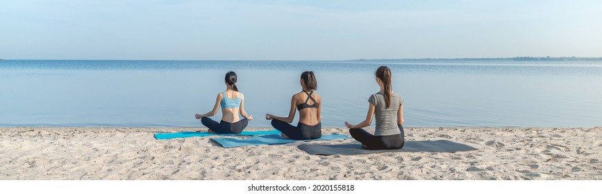 Panoramic shot of women making yoga meditation in lotus pose on sunny beach outdoor. Young sportswomen athletes sitting in lotus position together. Yoga training class - Powered by Shutterstock
