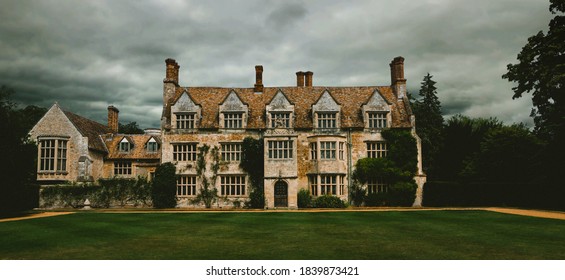 Panoramic, spooky old english manor house with lawn trees. Dramatic cloudy and overcast sky 
