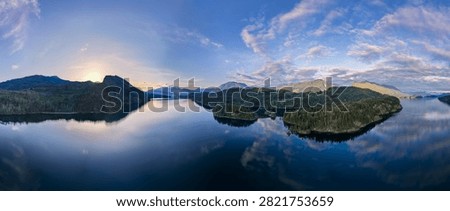 Panoramic sunrise over Harrison Lake with mirrored water, forested islands and mountains near Harrison Hot Springs, British Columbia, Canada.