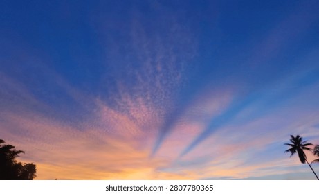 Panoramic sunset landscape capturing distinct shadow bands and light rays spreading through thin clouds during twilight hours