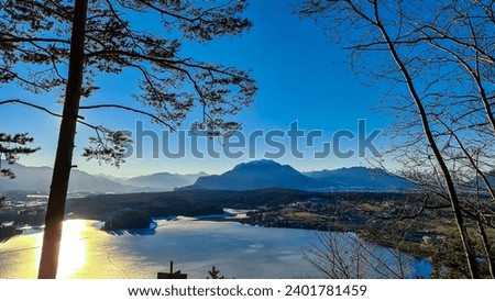 Panoramic sunset view on Lake Faak from Taborhoehe in Carinthia, Austria, Europe. Surrounded by high snow capped Austrian Alps mountains. Surface of lake is frozen. Alpine Landscape in frosty winter