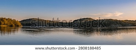 Panoramic sunset view over a calm lake with forested hills in Finland.