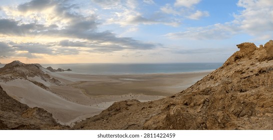 Panoramic sunset view over the remote sandy shoreline of Shoab Beach on Socotra Island, Yemen, with dramatic cliffs and the Arabian Sea.