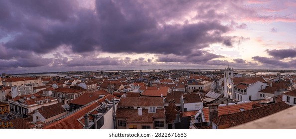 Panoramic sunset view over the rooftops of Aveiro, Portugal, captured from a high vantage point. The illuminated historic center, church steeples, salt marshes, and Aveiro lagoon create a stunning cityscape during the blue hour.
