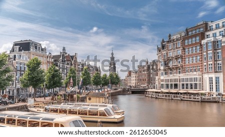 Panoramic timelapse hyperlapse of Amsterdam city center featuring Amstel River, waterfront and Munttoren tower. Boats float back and forth under cloudy sky. Scenic urban view from bridge. Netherlands