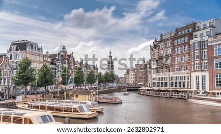 Panoramic timelapse hyperlapse of Amsterdam city center featuring Amstel River, waterfront and Munttoren tower. Boats float back and forth under cloudy sky. Scenic urban view from bridge. Netherlands