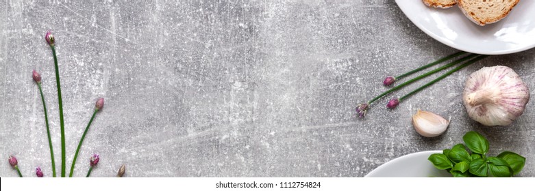 Panoramic Top View Of Gray Concrete Kitchen Counter Top With Bread On A White Plate, Garlic, Fresh Basil And Chive Flowers