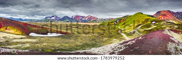 Panoramic unreal magic Icelandic landscape view\
of colorful rainbow volcanic Landmannalaugar mountains, red and\
pinky volcanic crater and famous Laugavegur hiking trail with\
dramatic sky, Iceland