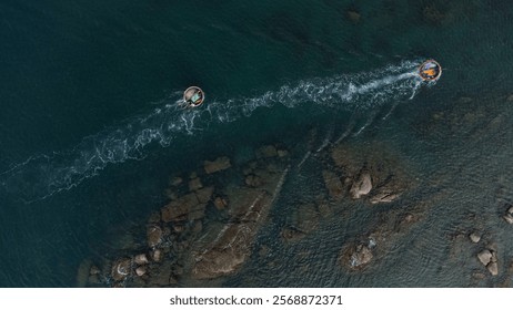 Panoramic view from above, looking down, two fishing boats racing to shore through the cliff, captured by flycam in Vietnam