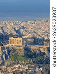 Panoramic view of the Acropolis and Parthenon in Athens, Greece, bathed in golden light, with the urban cityscape and sea in the background, showcasing history and modernity.