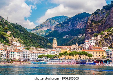 Panoramic view, aerial skyline of small haven of Amalfi village with tiny beach and colorful houses located on rock. Tops of mountains on Amalfi coast, Salerno, Campania, Italy.