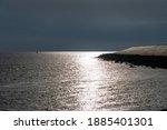 Panoramic view along one of the dikes on the north side of the island of Texel, The Netherlands, black storm clouds in the back while sun is glistening on water and concrete of the dike