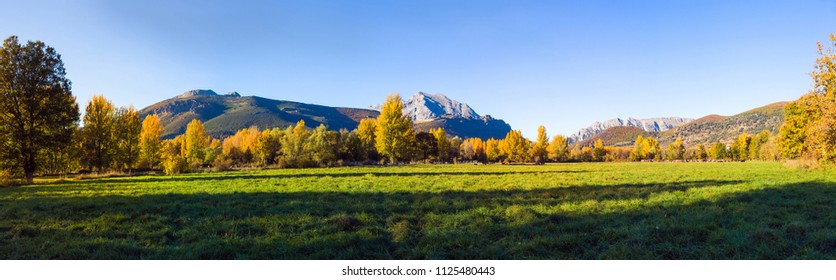 Panoramic view of autumnal landscape of green meadows groves and rocky mountains in the background. With small town hidden among the trees 