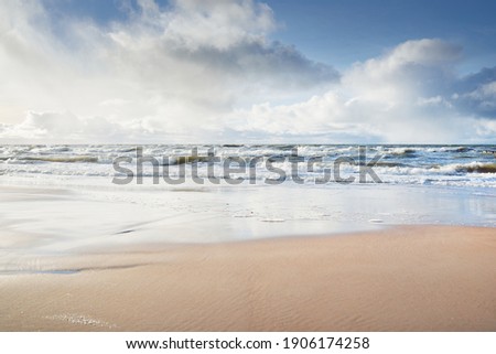 Panoramic view of Baltic sea from sandy shore (sand dunes). Dramatic sky with glowing clouds, sunbeams. Waves, water splashes. Idyllic seascape. Warm winter weather, climate change, nature. Denmark