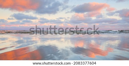 Panoramic view of the Baltic sea from a sandy shore. Clear sunset sky, colorful glowing pink clouds, soft light. Symmetry reflections on water, natural mirror. Weather, winter, climate change, nature