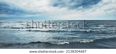 Panoramic view of the Baltic sea from a sandy shore (sand dunes). Dramatic sky with dark glowing clouds. Waves, water splashes. Idyllic seascape. Warm winter weather, climate change, nature
