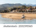 Panoramic view of the bay of the touristic village San Vicente de la Barquera at low tide and with seagulls on the sandy bottom next to a big boat on a sunny day in Cantabria.