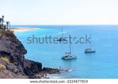 Panoramic view of the beach of Morro Jable with the turquoise sea full of sailboats and small boats sailing along the coast of Fuerteventura during a summer day with blue sky in the Canary Islands.