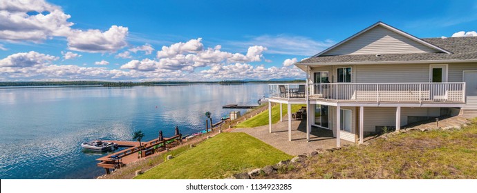 Panoramic View Of A Beautiful, Large Modern Luxury Summer Holiday Home, Featuring Sun Decks, Glass Railings, And Large Windows, Set Beside A Small Lake In Central British Columbia, Canada.