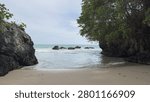 Panoramic view of a beautiful, secluded sandy beach, framed by towering rocky cliffs and lush green trees