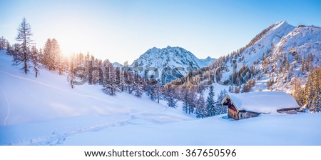 Panoramic view of beautiful winter wonderland mountain scenery with traditional mountain cabin the background in the Alps in golden evening light at sunset