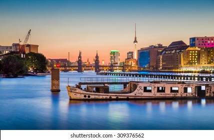 Panoramic view of Berlin skyline with famous TV tower and Oberbaum Bridge with old ship wreck lying in river Spree in twilight during blue hour at dusk, Berlin Friedrichshain-Kreuzberg, Germany