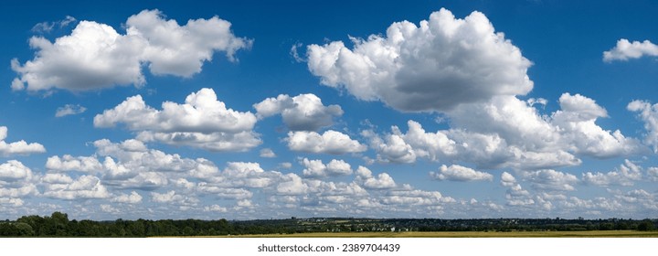 Panoramic view of the blue sky slightly overcast with cumulus clouds, cumulus clouds or fair weather clouds and fleecy clouds above the horizon with houses, fields and woodland - Powered by Shutterstock