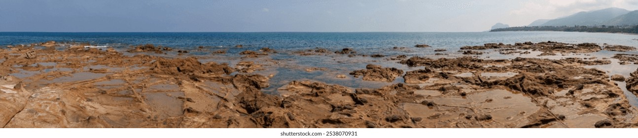 A panoramic view capturing a rocky coastline, calm sea, and distant hills under a clear sky. The expansive scene highlights the natural beauty and rugged terrain of the coastal landscape - Powered by Shutterstock