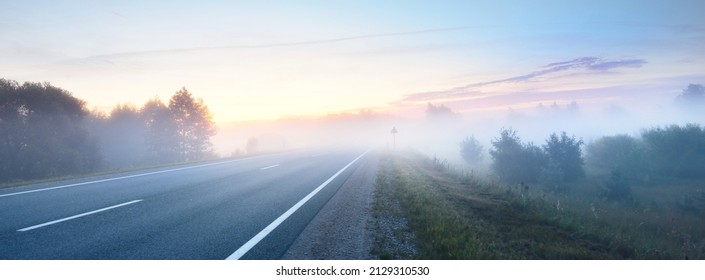 Panoramic view from the car of the empty highway through the fields and forest in a fog at sunrise. Europe. Transportation, logistics, travel, road trip, freedom, driving. Rural scene