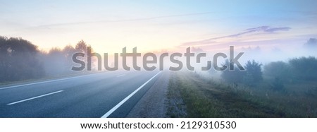 Panoramic view from the car of the empty highway through the fields and forest in a fog at sunrise. Europe. Transportation, logistics, travel, road trip, freedom, driving. Rural scene