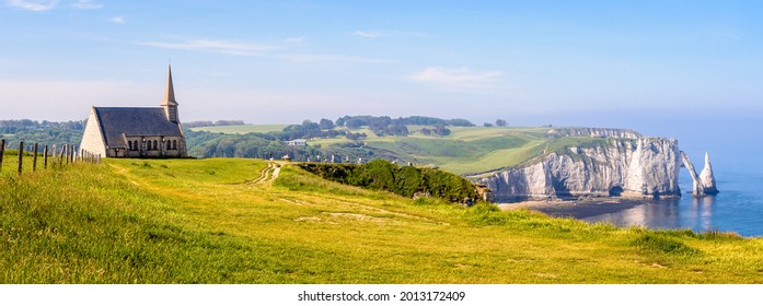 Panoramic view of the cliffs in Etretat, Normandy, with Notre-Dame de la Garde chapel overlooking the bay and the Aval cliff, its arch and the Needle in the distance. - Shutterstock ID 2013172409