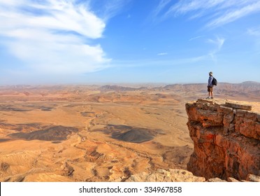 Panoramic view of color stone desert of Negev and traveler on the mountain top. National geological park HaMakhtesh HaGadol - Large Crater - a geological erosion land form, Israel