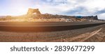 Panoramic View of a Desert Landscape With Dramatic Rock Formations and Clear Skies. Vast desert landscape showcases unique rock formations under a clear sky. The empty road stretches toward the horizon, inviting adventure through this stunning terrain.